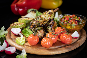 Grilled turkey skewers, skewered on wooden skewers, in a large plate decorated with herbs, zucchini and tomatoes.