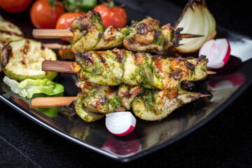 Grilled turkey skewers, skewered on wooden skewers, in a large plate decorated with herbs, zucchini and tomatoes.