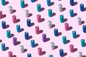 Pattern from spools of threads of different colors on a pink background.