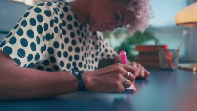 Serious biracial woman in notebook draws line up which symbolizes achievement of goals. Close up of young african american woman with pink marker draws graph while sitting at her workplace in office.