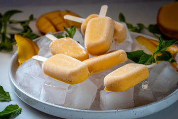 Ice cream sorbet from mango and banana. Ice cream on a stick in a large plate with ice cubes, garnished with mint and mango.