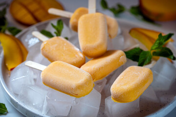 Ice cream sorbet from mango and banana. Ice cream on a stick in a large plate with ice cubes, garnished with mint and mango.