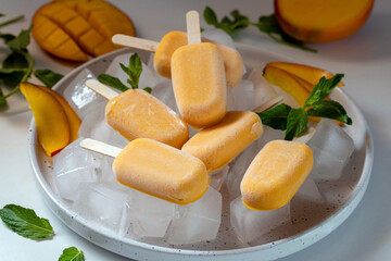 Ice cream sorbet from mango and banana. Ice cream on a stick in a large plate with ice cubes, garnished with mint and mango.