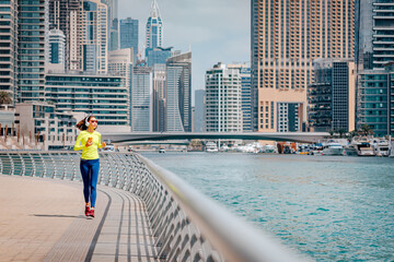 Happy woman wearing headphones and sunglasses trains and does running and fitness on the sidewalk...