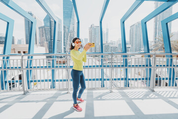 Woman in bright sportswear takes a selfie photo for her social networks while jogging through the streets of the city