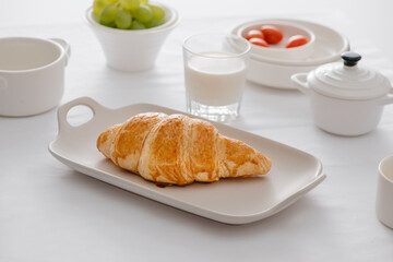 Breakfast served with croissants, fresh grapes, eggs, tomato, milk, butter and orange jam