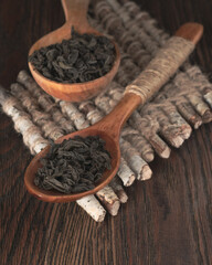 Wooden spoons with black tea leaves lying on a stand with birch twigs on the background of a textured table.
