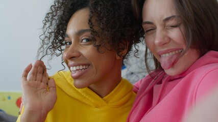 Two female friends fooling around at home. Black girl and caucasian young woman hugging. Happy girls taking selfie on the phone. Shot from the side of the camera very close