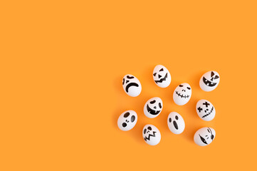 Minimal Halloween concept with white eggs as ghost characters on orange background. Flat lay