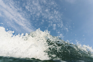 Wave breaking into the camera with blue sky and clouds above