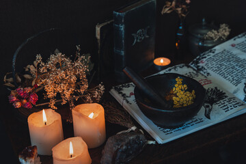 Wiccan witch altar prepared for casting a spell with an open Book of Shadows and pestle and mortar. Old spell books, crystals, burning lit candles, dried flowers in dark night background - obrazy, fototapety, plakaty