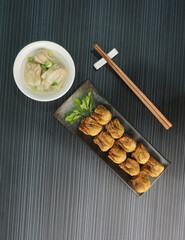 handmade deep fried and boiled pork meat dumpling wanton soup in plate on dark grey wood table asian dim sum halal food restaurant cuisine banquet menu for cafe