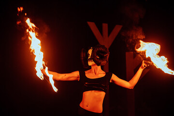 a fireshow artist in a mask of a mythical creature performs with fire. street culture festival. colorful mystical fire show at night