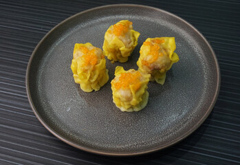 Chinese handmade classic steamed fresh yellow stew mai dumpling wrapped with pork and fish roe caviar in plate on dark grey wood table asian dim sum halal food restaurant cuisine banquet menu for cafe