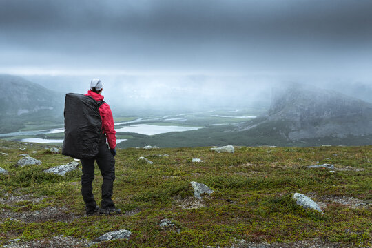 Female hiker overlooking Rapa river valley in rough arctic landscape of Sarek National Park, Sweden, on a very cloudy and rainy day. Hiking in the far north behind the arctic circle.