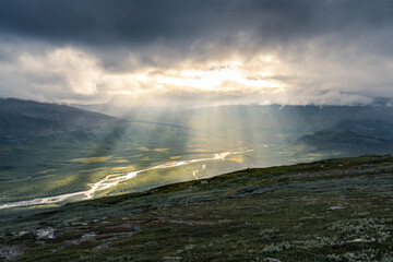 Naklejka na ściany i meble Remote harsh arctic landscape in rough weather in Sarek national park, Swedish Lapland. Heavy clouds with rays of light coming through.