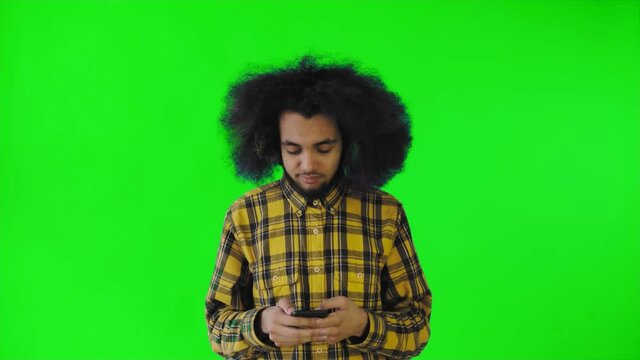 A young man with an African hairstyle on a green background is talking into his phone.