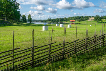 Small settlement farm in sourthern Sweden on a beautiful sunny summer day. Holiday in Swedish countryside. Vintage fence and white heystacks.