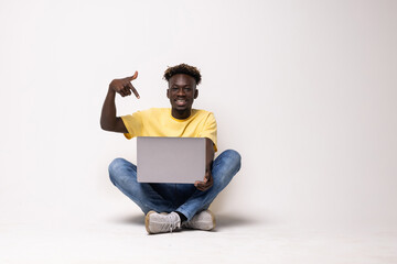 Young african man sitting on the floor with a laptop person pointing by hand to a shirt copy space, proud and confident