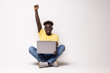 Young smiling african man standing and using laptop computer isolated over gray background