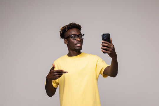 young afro man smiling happy taking selfie self portrait picture with mobile phone looking excited having fun posing cool isolated in grey background