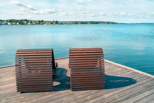 Two wooden beach beds or chairs on a wooden pier next to the sea with cityscape in the background. Sunny summer day by the Baltic Sea in Vastervik, southern Sweden. Summer vacation by the sea.
