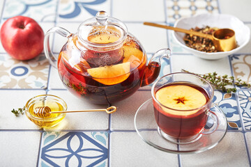 Fruit tea with apples and thyme in glass teapot and cup on table made of colored tiles