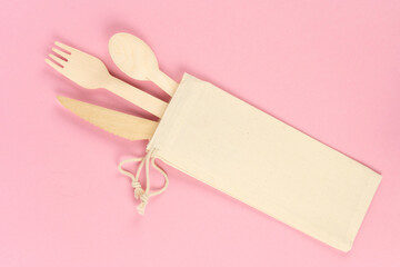 Wooden disposable set of cutlery for food in a bag, on a colored background, dishes Eco.