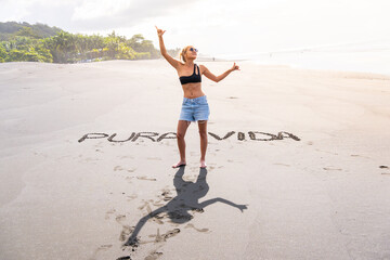 Blonde woman on a beach with inscriptions in the sand gesturing to be happy