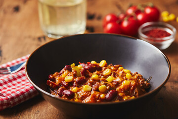 Chili Con Carne with ground beef, beans and corn in dark bowl on wooden background. Mexican and Texas cuisine