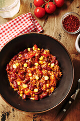 Chili Con Carne with ground beef, beans and corn in dark bowl on wooden background. Mexican and Texas cuisine