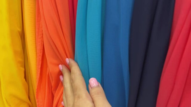 4k Multicoloured fabric in a textile shop. Female hand touches the fabrics.