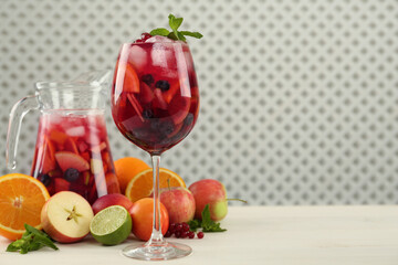 Glass and jug of Red Sangria with fruits on white wooden table, space for text