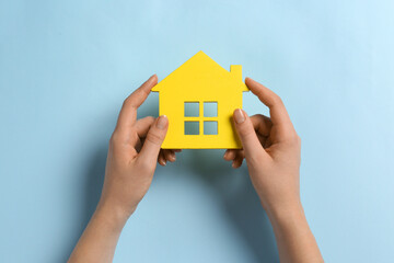 Woman holding house figure on light blue background, top view