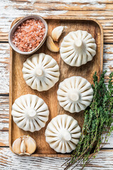 Fototapeta na wymiar Frozen Raw dumplings Khinkali with beef and lamb meat on wooden tray with herbs. White wooden background. Top view
