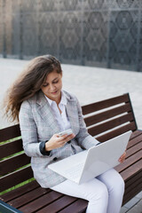 woman sitting on a bench working on laptop and mobile phone