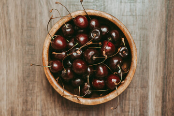 Ripe red cherries in a wooden cup on a wooden table