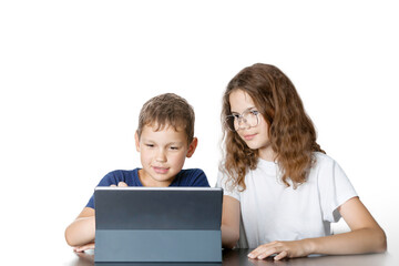The interested brunettes boy and girl in glasses are sitting at the table by the tablet on isolated white background.  The concept of distance learning, interaction, communication.