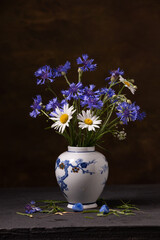 Bouquet of wild flowers in a porcelain vase on a dark background