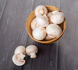 Young fresh mushrooms in a wooden bowl on a dark wood background