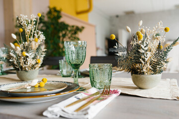 Rustic dining table setting: dried flowers in a vase, green glass glasses and ceramic plates