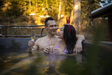 Happy mixed race couple in jacuzzi swimming pool on resort spa pampering romantic weekend getaway for honeymoon vacation during winter, Asian woman and caucasian man drink champagne for christmas.