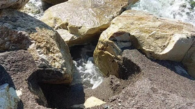movimiento de las olas en la playa rompiendo sobre unas rocas y salpicando con la espuma.