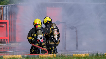 Two firefighters sit and spray water from fire hose during practice or training the process to extinguish fire in real life.