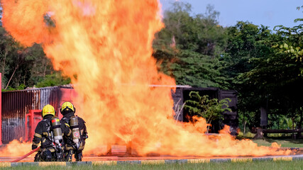 Two fireman sit in front of big fire outdoor during practice or training to extinguish fire and...