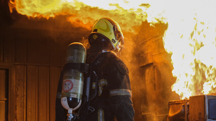 Back of fireman with protective suit stand and look at fire on wall of kitchen room during practice or training staff for preparation and ready to work as professional.