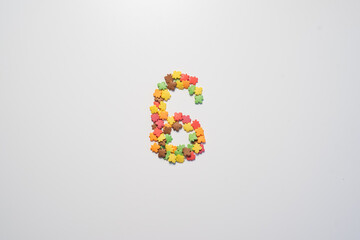 Number six from sweet pastry topping in the form of colorful foliage on a white background.