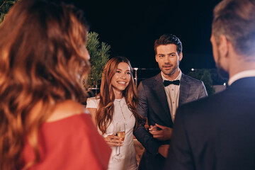Group of people in formalwear communicating and smiling while spending time on luxury party
