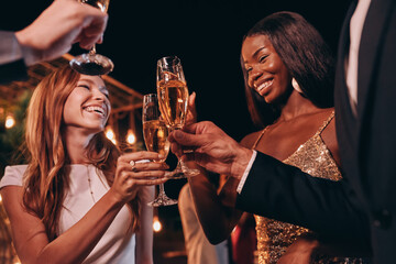 Group of people in formalwear toasting with champagne and smiling while spending time on luxury party