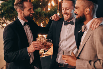 Three men in suits and bowties drinking whiskey and communicating while spending time on party